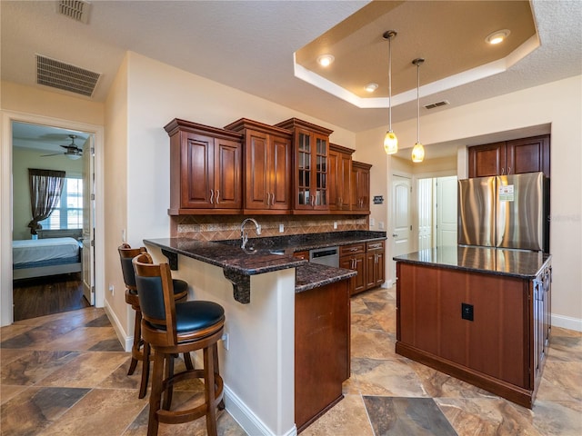 kitchen with dark stone countertops, pendant lighting, a raised ceiling, appliances with stainless steel finishes, and ceiling fan