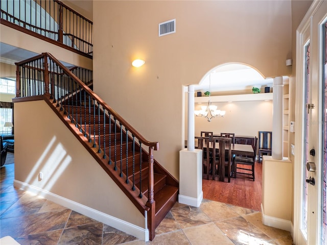 stairs featuring decorative columns, an inviting chandelier, and a high ceiling