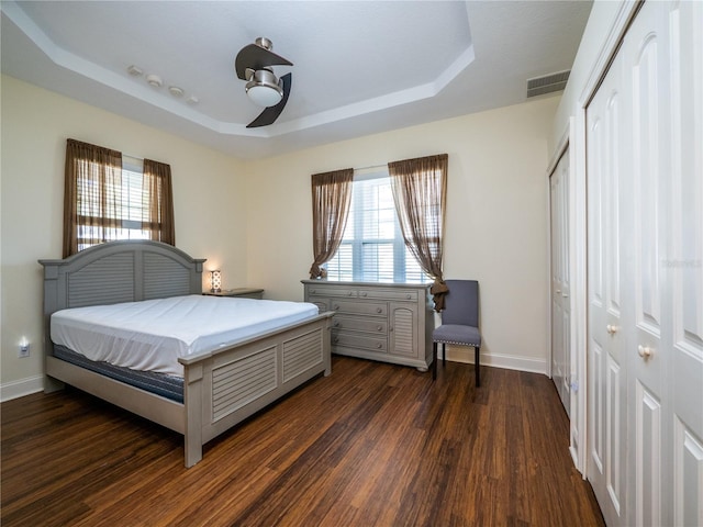 bedroom with dark hardwood / wood-style floors, a tray ceiling, and ceiling fan