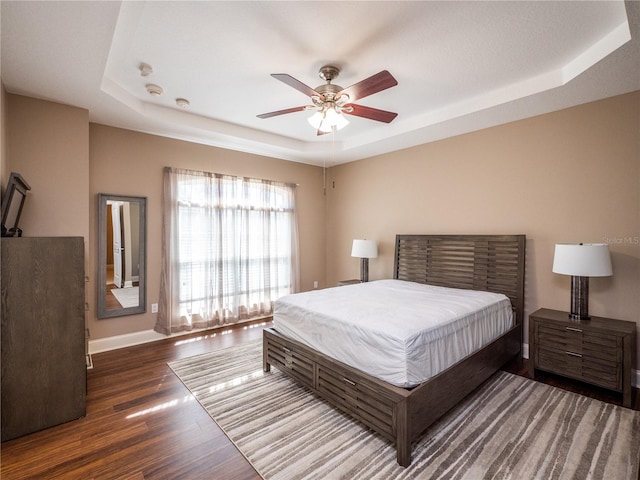 bedroom featuring ceiling fan, dark hardwood / wood-style floors, and a raised ceiling