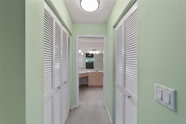 corridor with a textured ceiling, sink, and carpet flooring