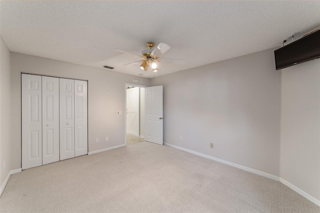 unfurnished bedroom with light colored carpet, a closet, ceiling fan, and a textured ceiling