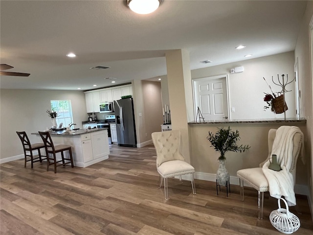 kitchen featuring a kitchen breakfast bar, appliances with stainless steel finishes, kitchen peninsula, hardwood / wood-style flooring, and white cabinets