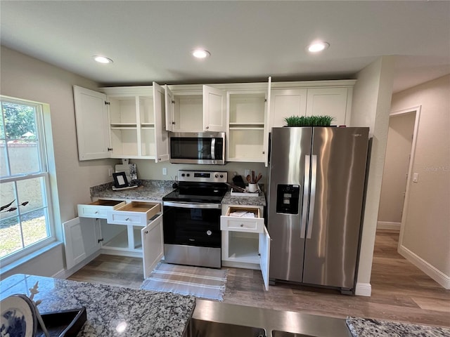 kitchen with appliances with stainless steel finishes, light hardwood / wood-style floors, white cabinets, and light stone countertops