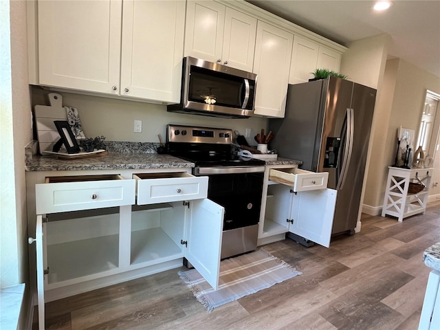 kitchen with appliances with stainless steel finishes, white cabinets, light stone countertops, and wood-type flooring