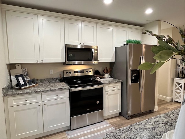 kitchen with stone counters, light wood-type flooring, appliances with stainless steel finishes, and white cabinetry