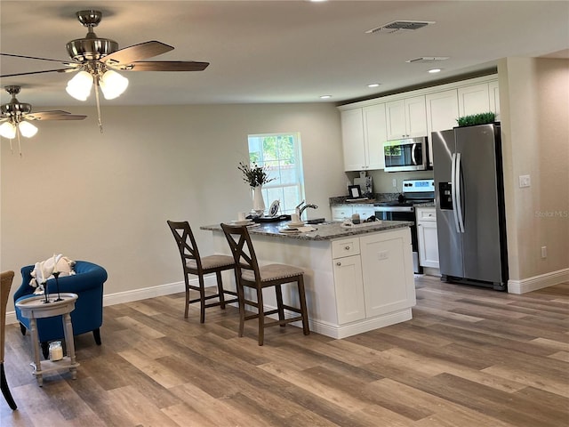 kitchen featuring stainless steel appliances, white cabinetry, hardwood / wood-style flooring, and dark stone counters