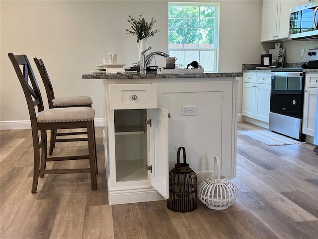 kitchen with white cabinetry, dark stone countertops, light hardwood / wood-style floors, and appliances with stainless steel finishes