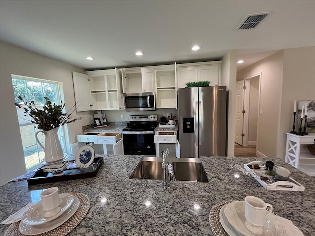 kitchen with white cabinets, stainless steel appliances, dark stone counters, and sink