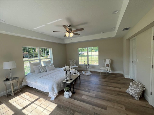 bedroom with ceiling fan, dark wood-type flooring, and a tray ceiling