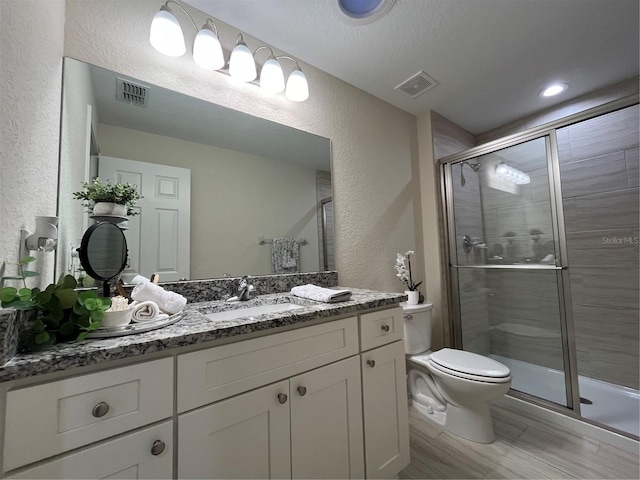 bathroom featuring a textured ceiling, a shower with shower door, vanity, and toilet