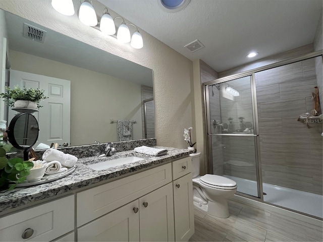 bathroom featuring toilet, a textured ceiling, walk in shower, and vanity