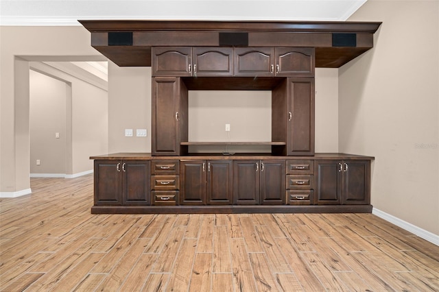 bar with dark brown cabinetry, light hardwood / wood-style flooring, and ornamental molding