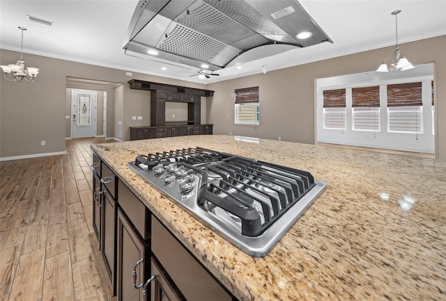 kitchen with stainless steel gas stovetop, ventilation hood, ceiling fan with notable chandelier, crown molding, and wood-type flooring