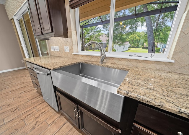 kitchen featuring light stone countertops, dark brown cabinets, light wood-type flooring, and stainless steel dishwasher