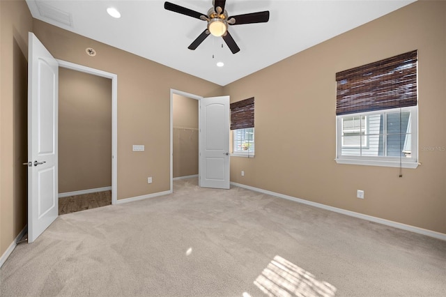 unfurnished bedroom with ceiling fan, light colored carpet, a walk in closet, and multiple windows