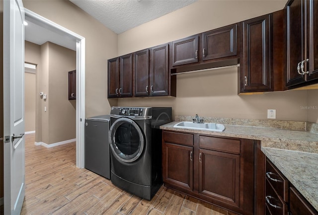 laundry room featuring sink, cabinets, light hardwood / wood-style flooring, a textured ceiling, and washer and dryer