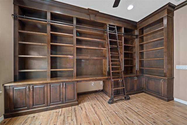 unfurnished office featuring ceiling fan, built in desk, a textured ceiling, and light hardwood / wood-style flooring