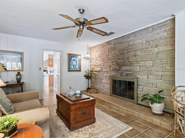 tiled living room featuring a stone fireplace, ceiling fan, and a textured ceiling