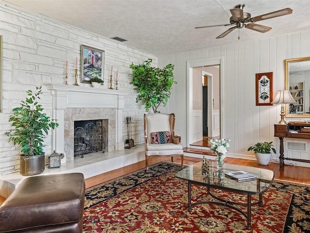 living room featuring wood-type flooring, ceiling fan, a high end fireplace, and a textured ceiling