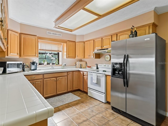 kitchen with appliances with stainless steel finishes, tile counters, sink, and light tile floors