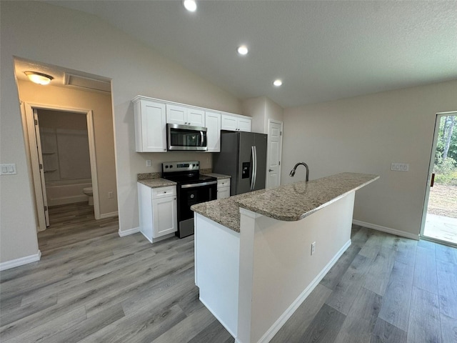 kitchen with light hardwood / wood-style floors, vaulted ceiling, a kitchen island with sink, white cabinets, and appliances with stainless steel finishes