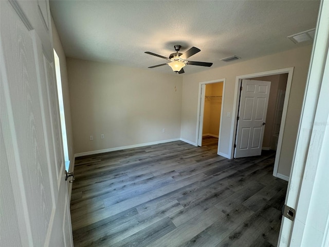 unfurnished bedroom featuring ceiling fan, wood-type flooring, a textured ceiling, a walk in closet, and a closet