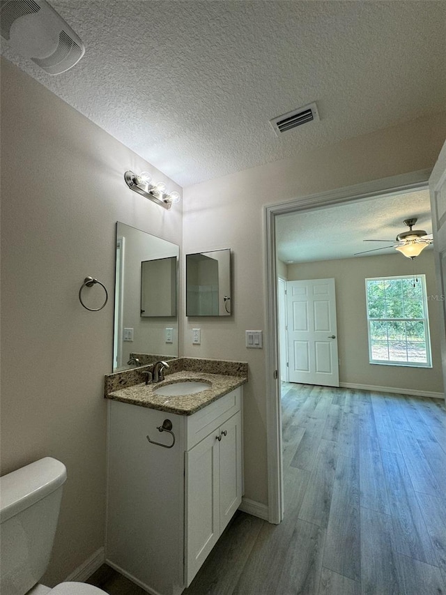 bathroom featuring ceiling fan, a textured ceiling, toilet, vanity, and hardwood / wood-style flooring