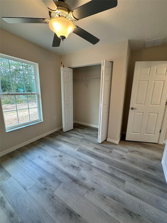 unfurnished bedroom featuring ceiling fan, a closet, a textured ceiling, and light hardwood / wood-style flooring