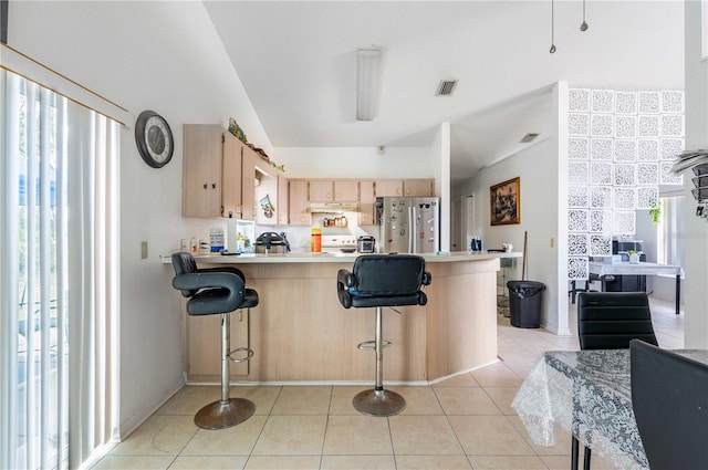 kitchen with kitchen peninsula, a healthy amount of sunlight, stainless steel fridge, and lofted ceiling