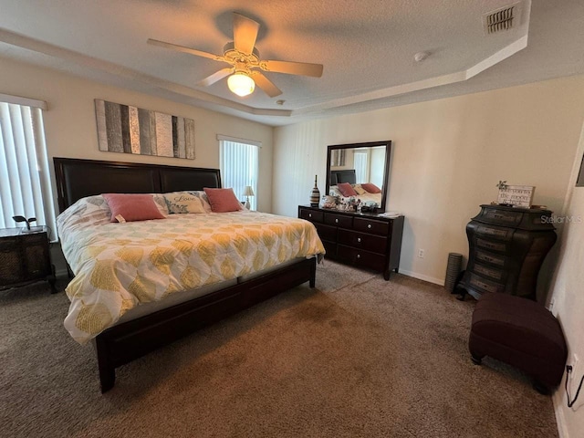 carpeted bedroom with ceiling fan, a tray ceiling, and a textured ceiling