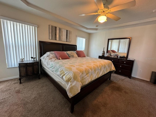 bedroom with ceiling fan, dark carpet, and a tray ceiling