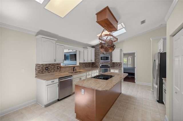 kitchen with vaulted ceiling, appliances with stainless steel finishes, a center island, white cabinets, and backsplash