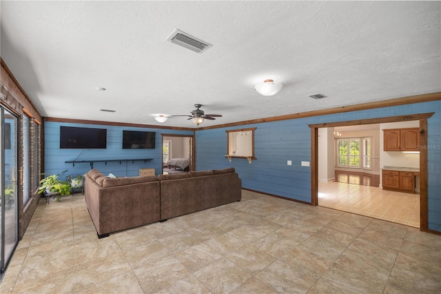 living room with ceiling fan, wood walls, a textured ceiling, and light tile patterned floors