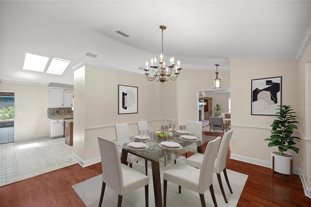 dining space with a notable chandelier, light wood-type flooring, crown molding, and vaulted ceiling with skylight