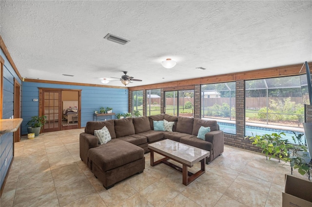 living room featuring ceiling fan, wooden walls, and a textured ceiling