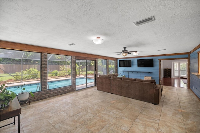 living room featuring ceiling fan, wood walls, light tile patterned floors, and a textured ceiling