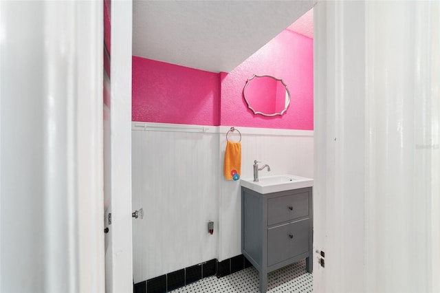 bathroom with a textured ceiling, vanity, and wood walls