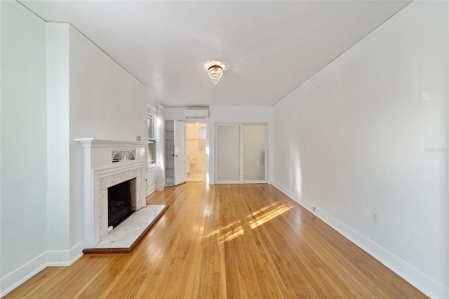 unfurnished living room featuring a wall mounted air conditioner, light wood-type flooring, and a premium fireplace