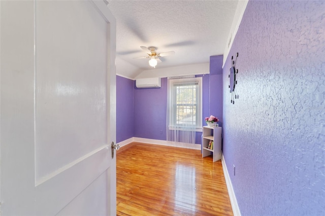 empty room with vaulted ceiling, ceiling fan, a textured ceiling, wood-type flooring, and a wall unit AC