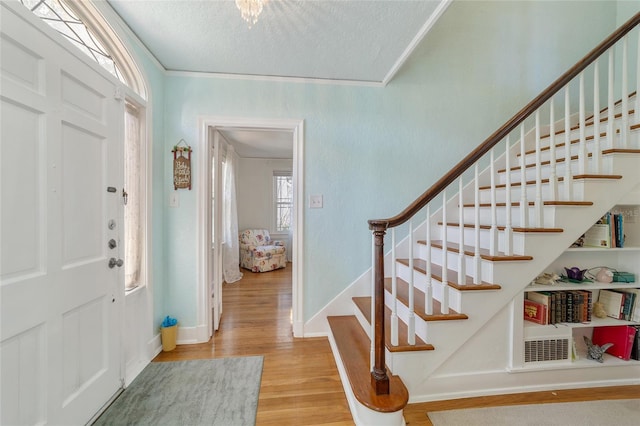 foyer featuring crown molding, a textured ceiling, and light hardwood / wood-style flooring