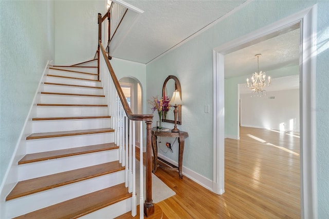 stairway with wood-type flooring and a notable chandelier