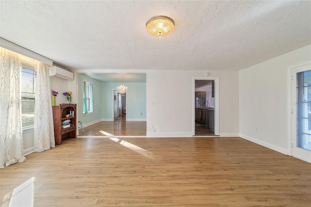 unfurnished living room featuring a textured ceiling, light wood-type flooring, an inviting chandelier, and a wall unit AC