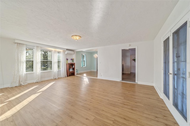 unfurnished living room with a textured ceiling, light hardwood / wood-style floors, an inviting chandelier, and a wall mounted AC