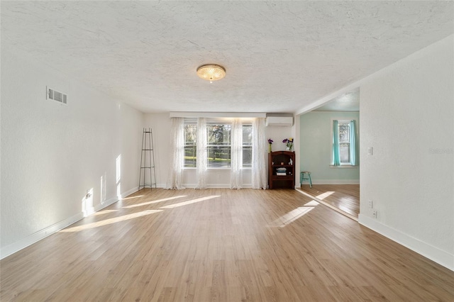 unfurnished living room featuring a wall unit AC, light hardwood / wood-style flooring, and a textured ceiling