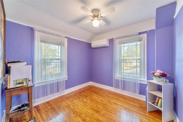 empty room featuring ceiling fan, a wall mounted AC, a textured ceiling, lofted ceiling, and hardwood / wood-style flooring