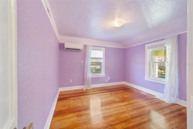 empty room featuring a textured ceiling, a wall mounted AC, wood-type flooring, and vaulted ceiling