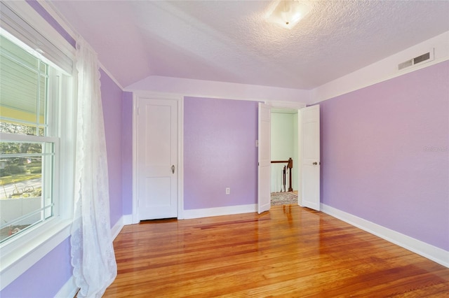 unfurnished bedroom featuring a textured ceiling, lofted ceiling, and light wood-type flooring