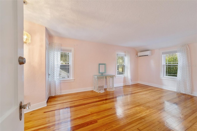 unfurnished living room with a wall mounted air conditioner, a textured ceiling, light hardwood / wood-style flooring, and a healthy amount of sunlight