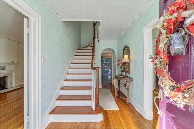 staircase featuring wood finished floors, a high end fireplace, arched walkways, crown molding, and baseboards